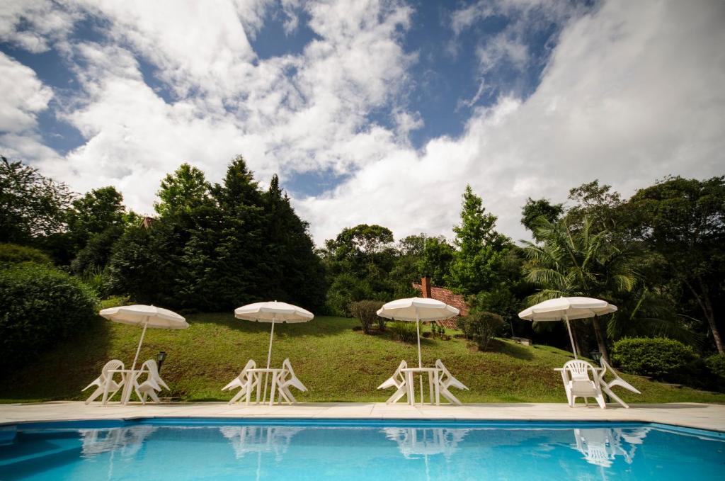 um grupo de cadeiras e guarda-sóis ao lado de uma piscina em Pousada Alpes em Santo Antônio do Pinhal