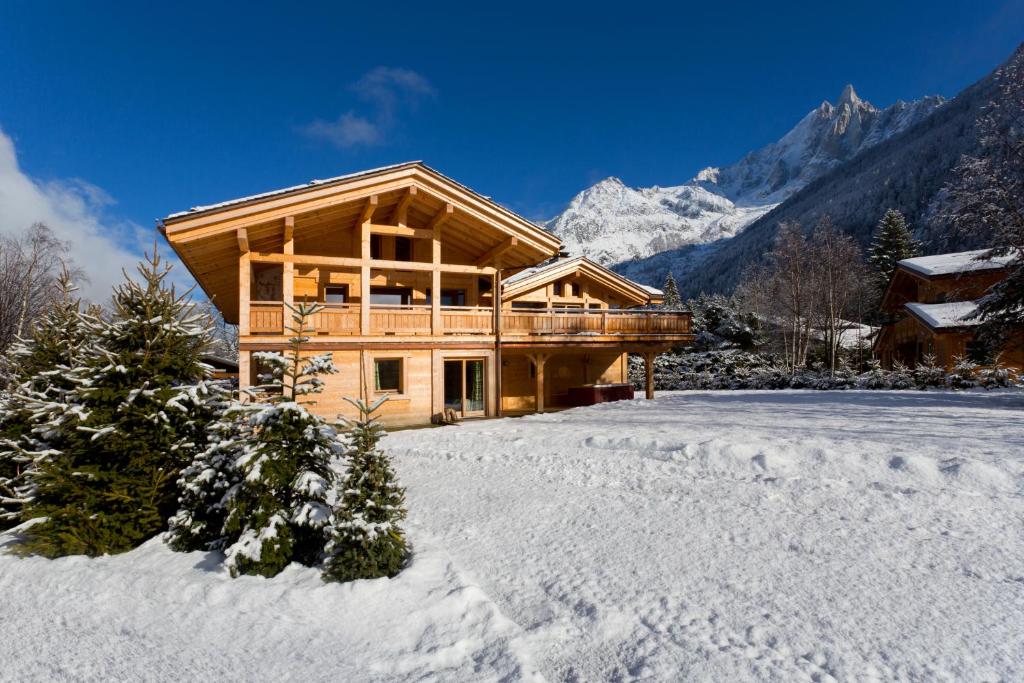 una cabaña de madera en la nieve con un patio cubierto de nieve en Chalet Isabelle Mountain lodge 5 star 5 bedroom en suite sauna jacuzzi, en Chamonix-Mont-Blanc