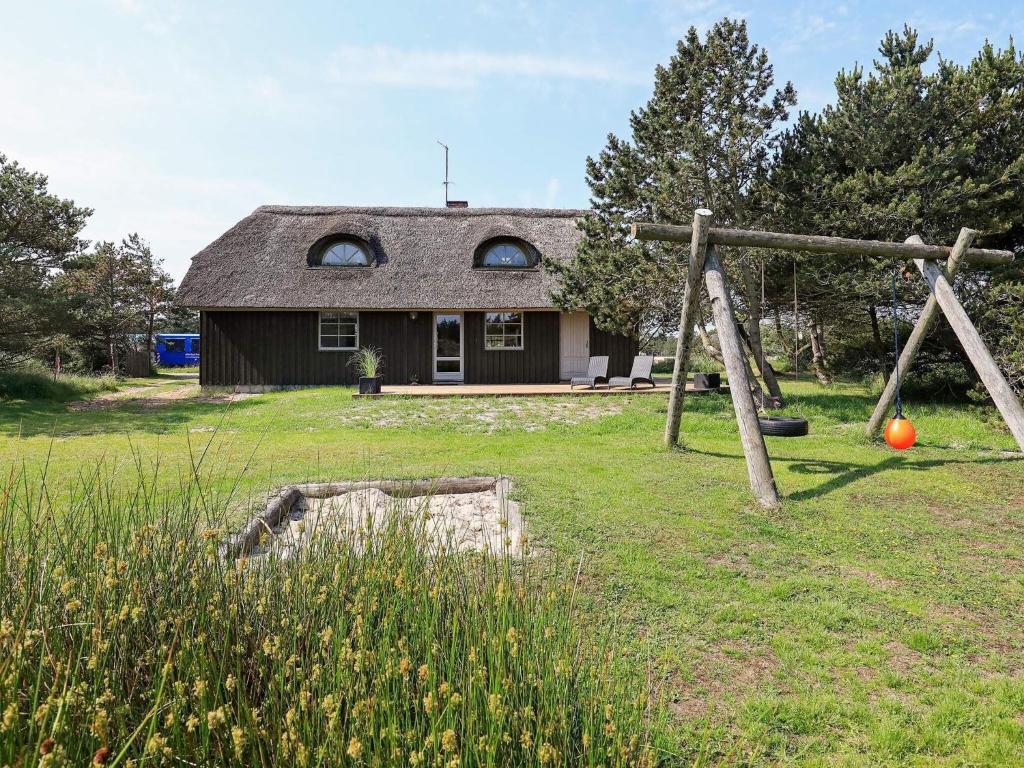 a yard with a swing in front of a house at 6 person holiday home in Bl vand in Blåvand
