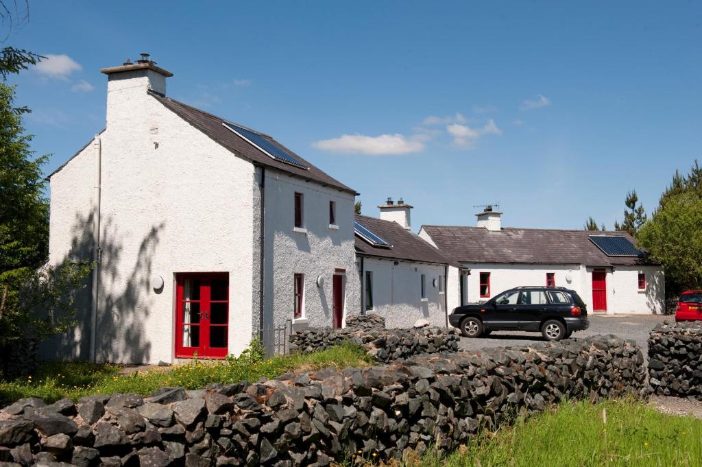 una casa blanca con puertas rojas y un coche aparcado delante en An Creagán Self Catering Cottages, en Greencastle