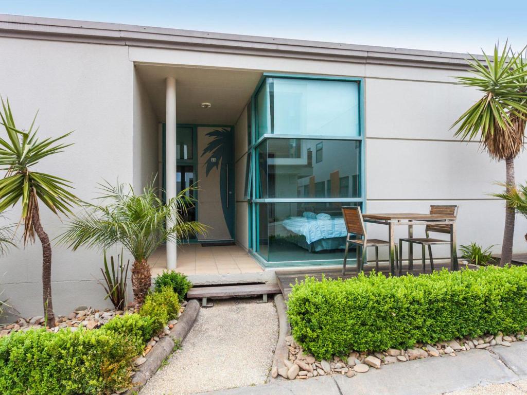 a house with a table and chairs and palm trees at Anglesea River Apartment 23 in Anglesea