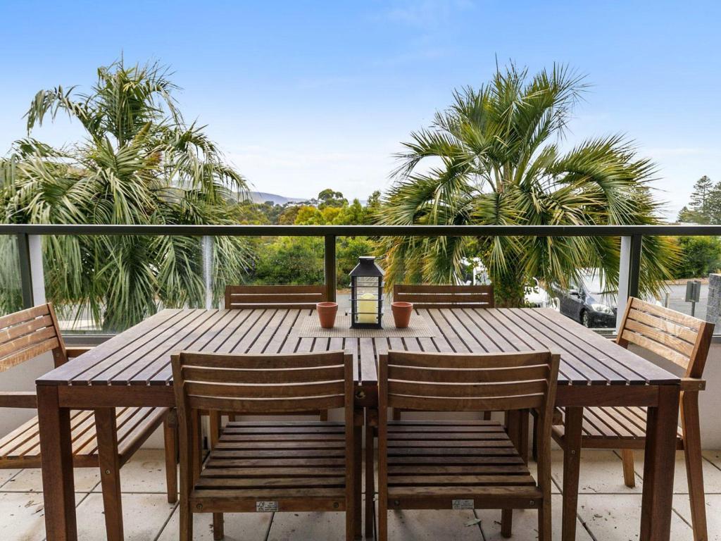 einen Holztisch und Stühle auf einem Balkon mit Palmen in der Unterkunft Lorne Chalet Apartment 11 Odyssea in Lorne