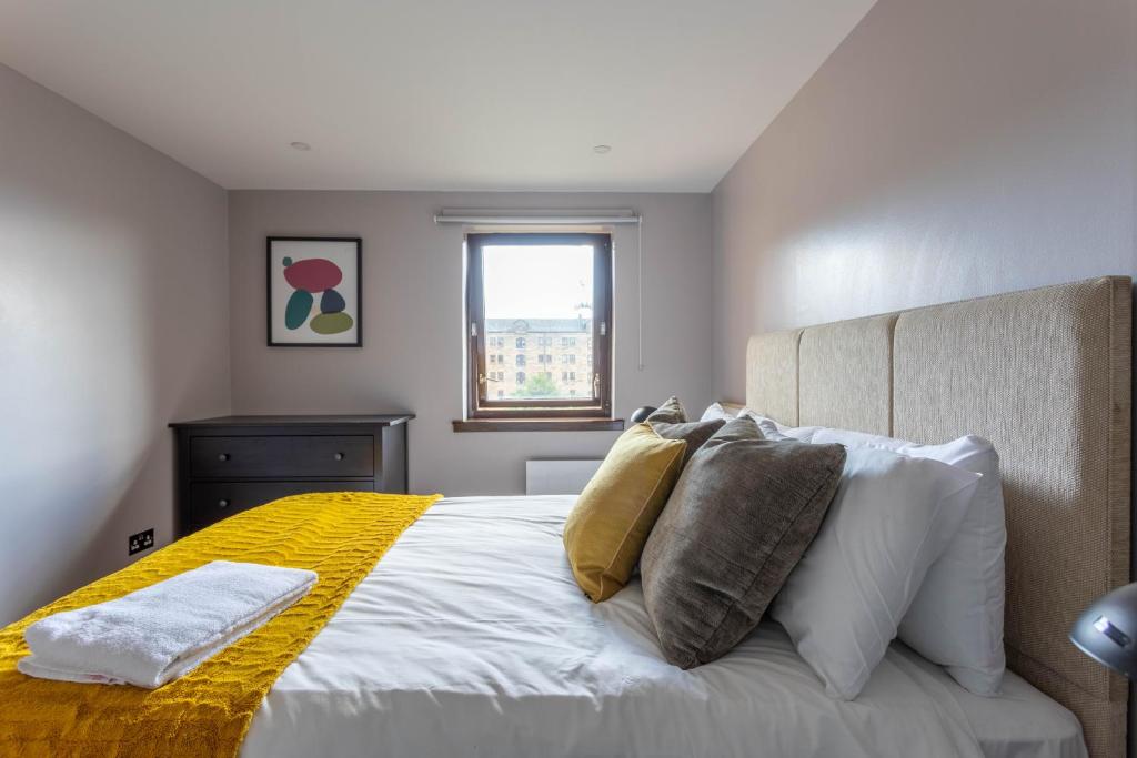 1 dormitorio con 1 cama blanca grande con manta amarilla en Stunning 1 Bed Merchant City Apartment with Parking en Glasgow