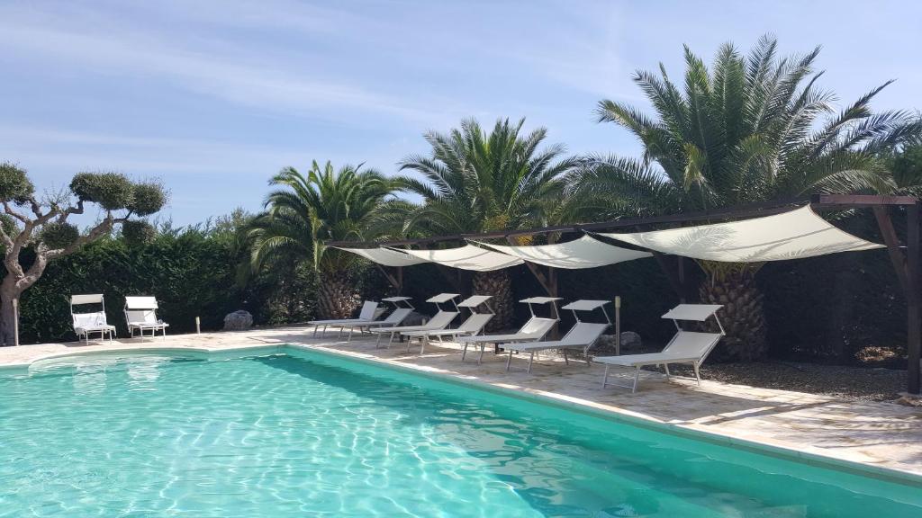 a swimming pool with chairs and a group of palm trees at Masseria Cesarina B&B in Castellana Grotte