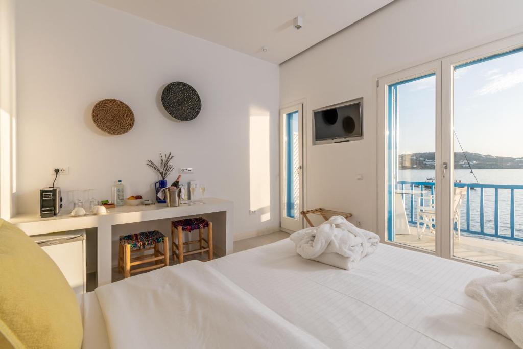 Dormitorio blanco con cama grande y vistas al océano en Bluetopia Suites, en Mykonos ciudad