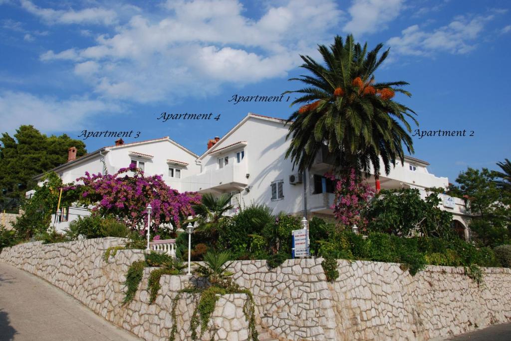 a white house with a palm tree behind a stone wall at Apartments & rooms Mila in Banjol