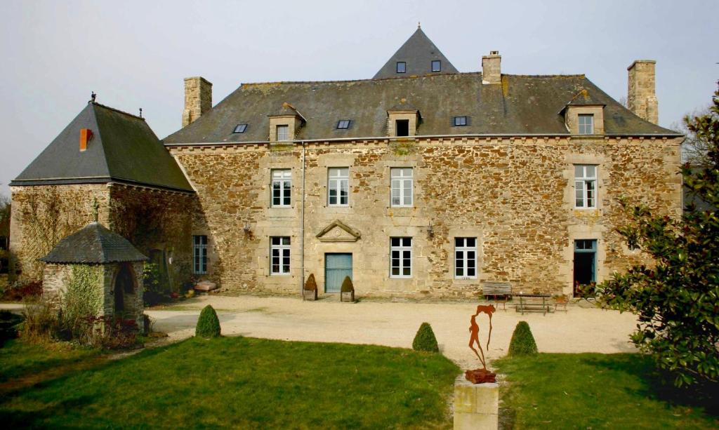 een groot stenen huis met een standbeeld ervoor bij Gîte La Passerelle - Manoir le Plessix Madeuc in Corseul