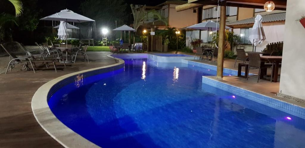 a swimming pool at night with tables and umbrellas at Village Duplex Confortável e Acolhedor junto a Natureza in Itacimirim