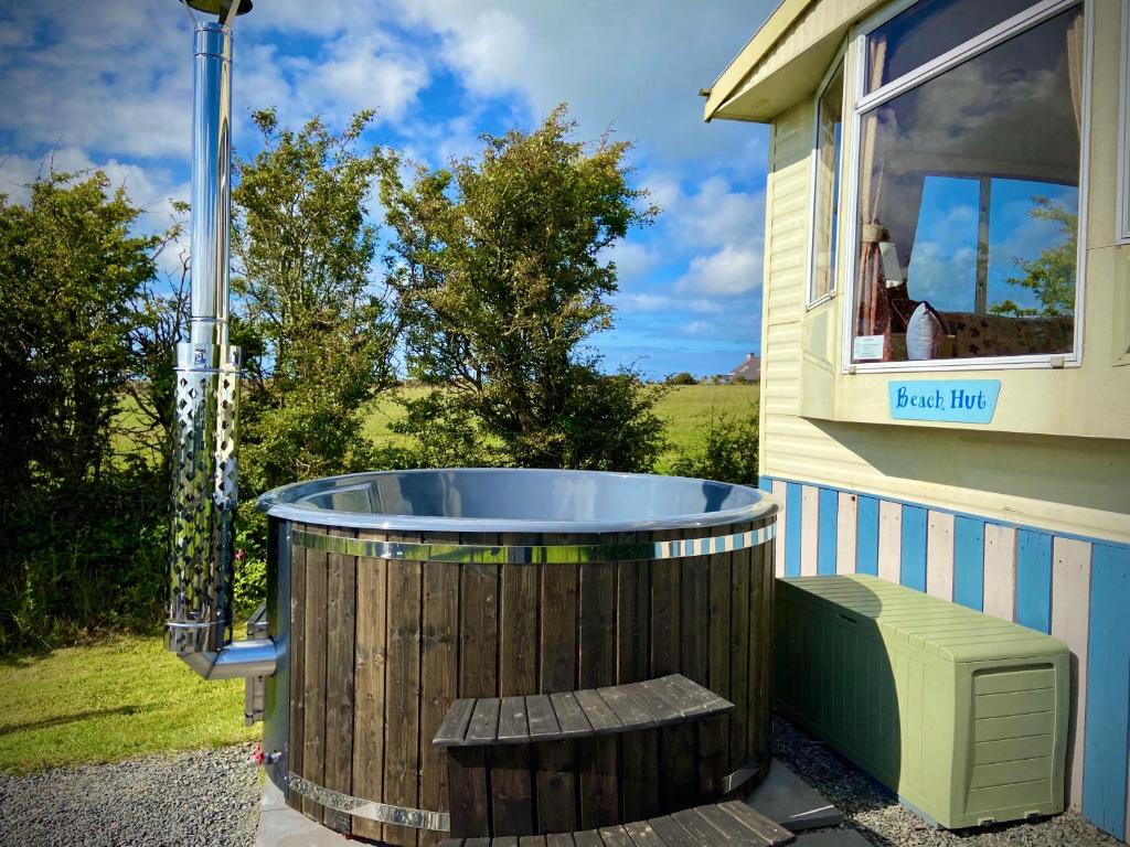 a large wooden tub sitting outside of a house at Glamping Huts x 3 and a Static Caravan available each with a Private Hot Tub, FirePit, BBQ and are located in a Peaceful setting with Alpacas and gorgeous countryside views on Anglesey, North Wales in Amlwch