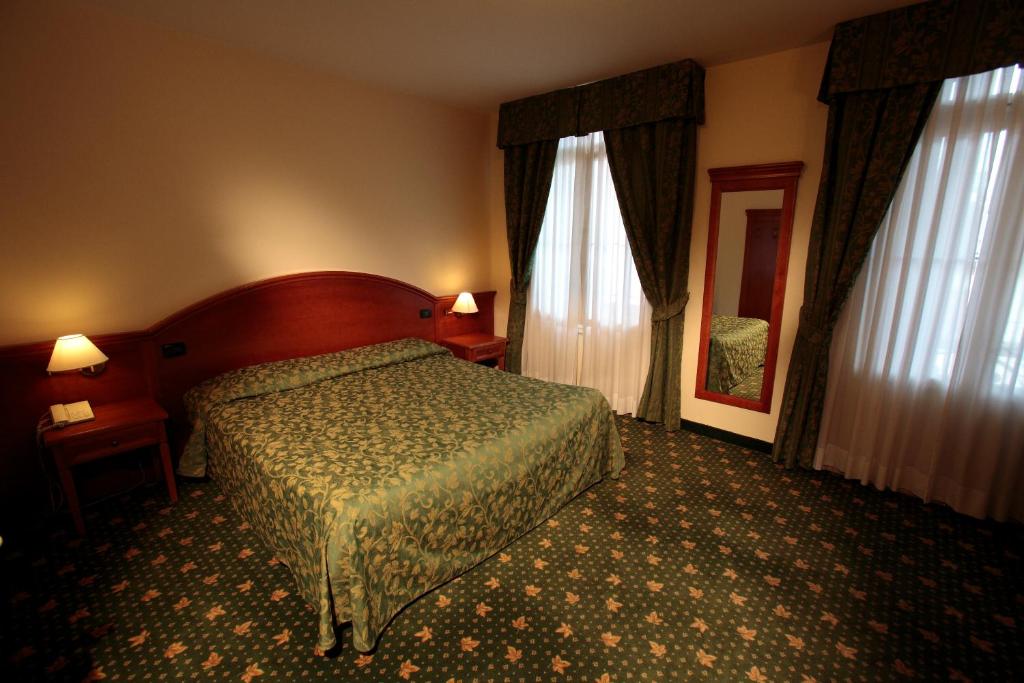a hotel room with a bed and two windows at Hotel Croce Bianca in Asiago