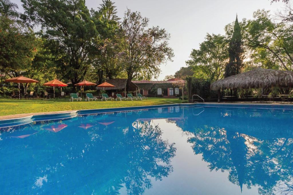 a swimming pool with chairs and umbrellas in a resort at Hotel Racquet Cuernavaca in Cuernavaca