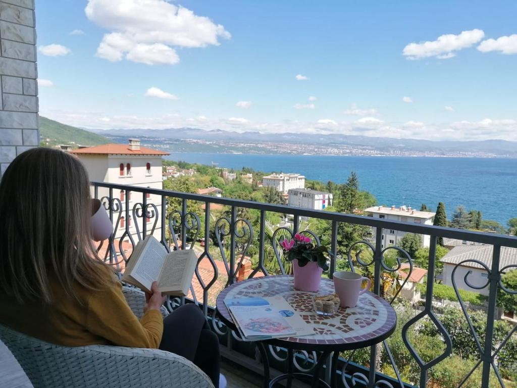 a woman sitting at a table reading a book on a balcony at Villa Allegra in Lovran