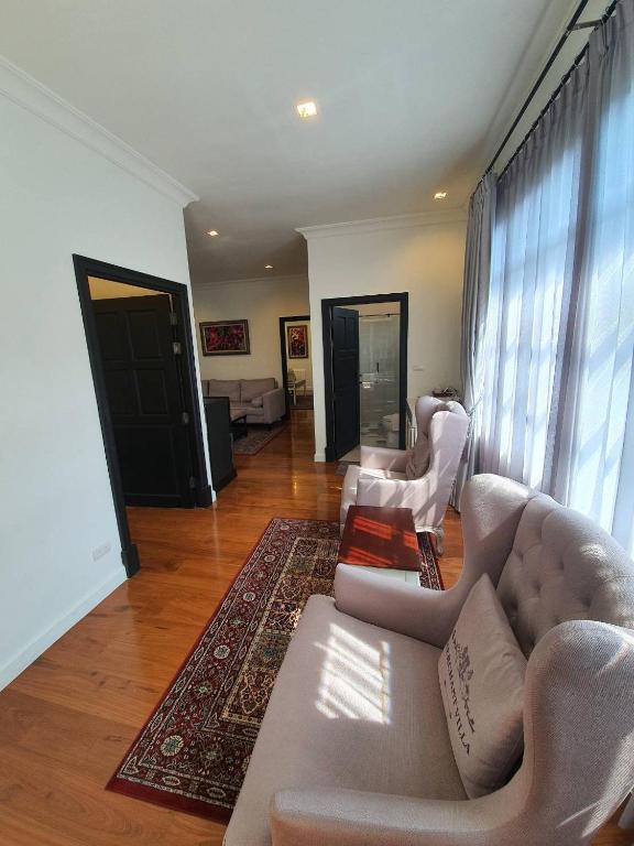 A sunlit sitting area with tufted armchairs, a patterned rug and a connecting room beyond.