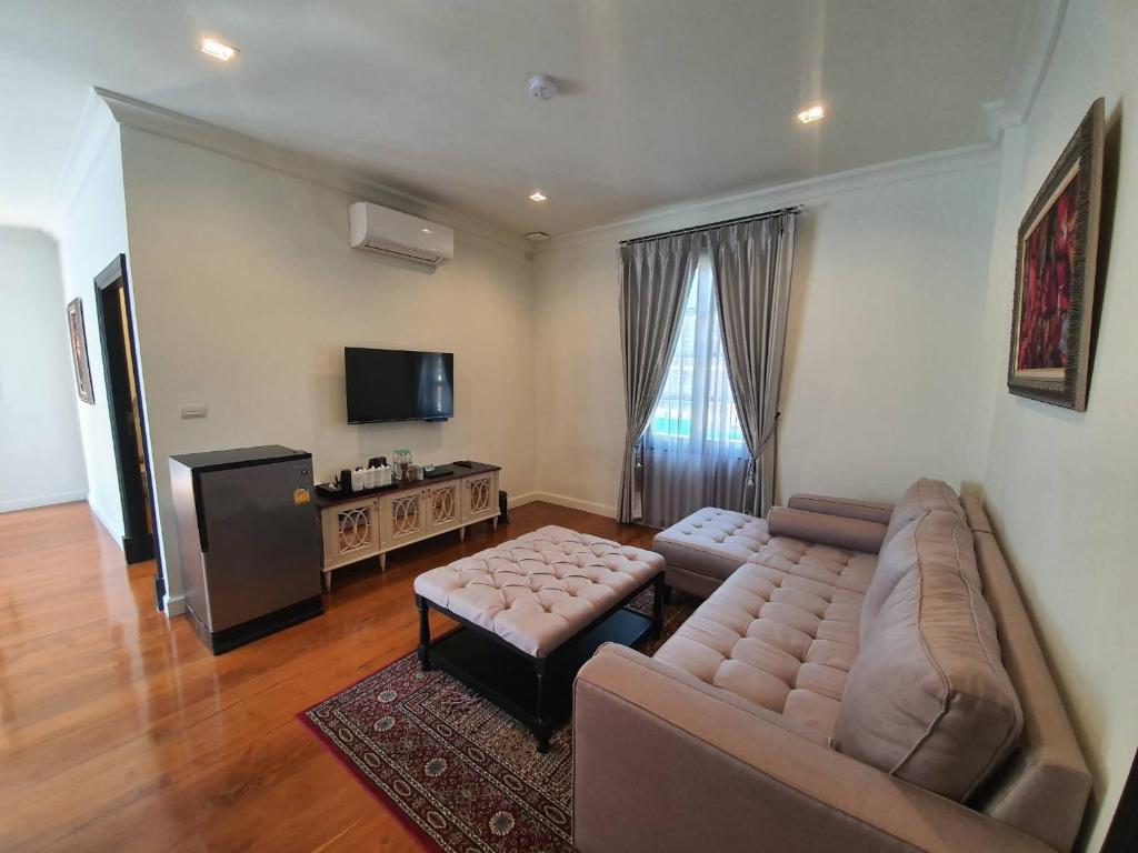 A large lounge with a sectional sofa, ottoman tables, television and curtained window.