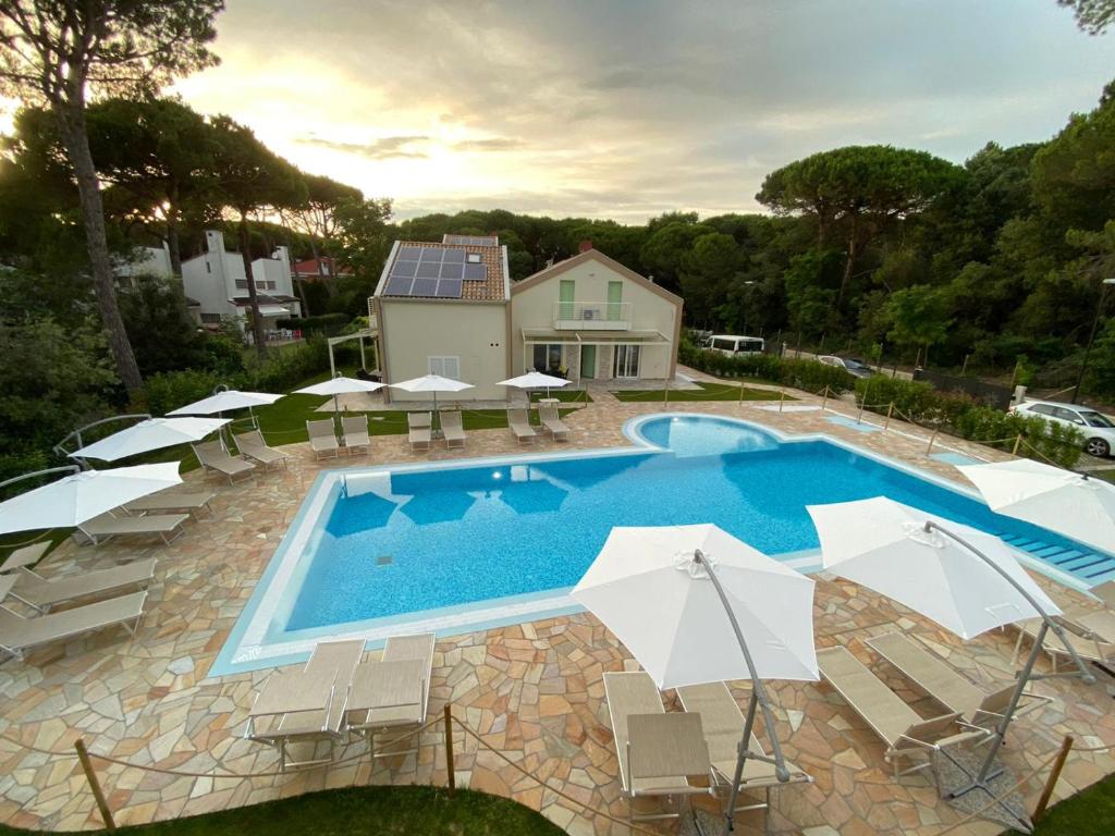 einen Pool mit Stühlen und Sonnenschirmen neben einem Haus in der Unterkunft Le Dune Verdi in Lido di Jesolo