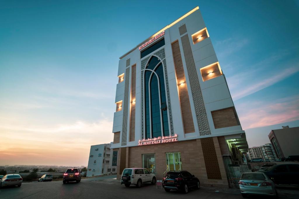 a building with cars parked in a parking lot at Alhattali Hotel in Muscat