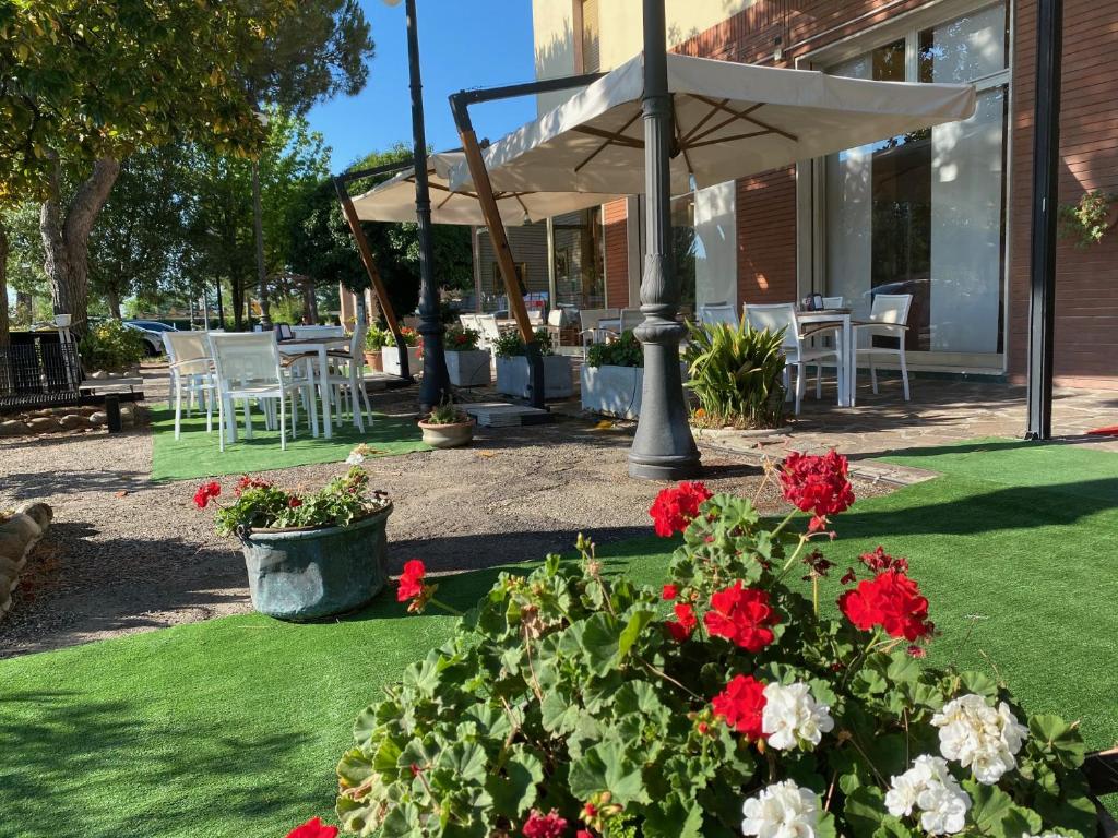 a patio with red and white flowers and an umbrella at Hotel Adriatico in Borgo Fosso Ghiaia