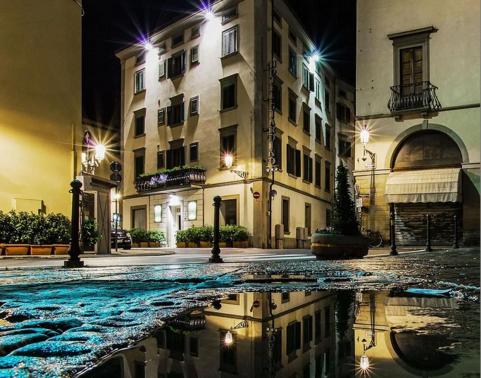 una strada di città di notte con un riflesso in una pozzanghera di Hotel Giardino a Prato