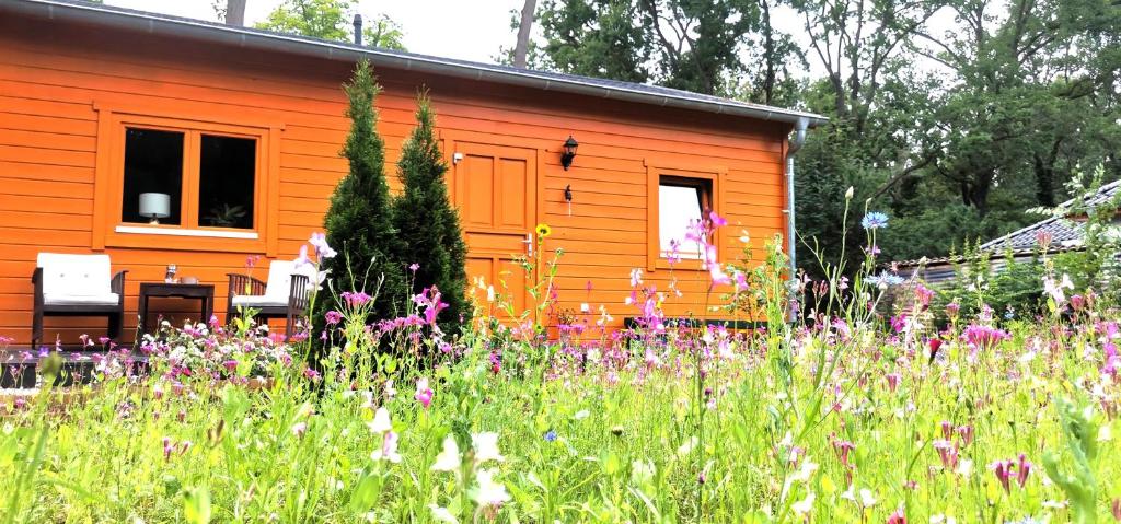 ein orangenes Haus mit einem Blumenfeld davor in der Unterkunft Blockbohlenhaus bei Potsdam in Schwielowsee