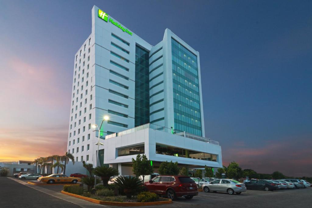un edificio alto con coches estacionados en un estacionamiento en Holiday Inn Queretaro Zona Krystal, an IHG Hotel, en Querétaro
