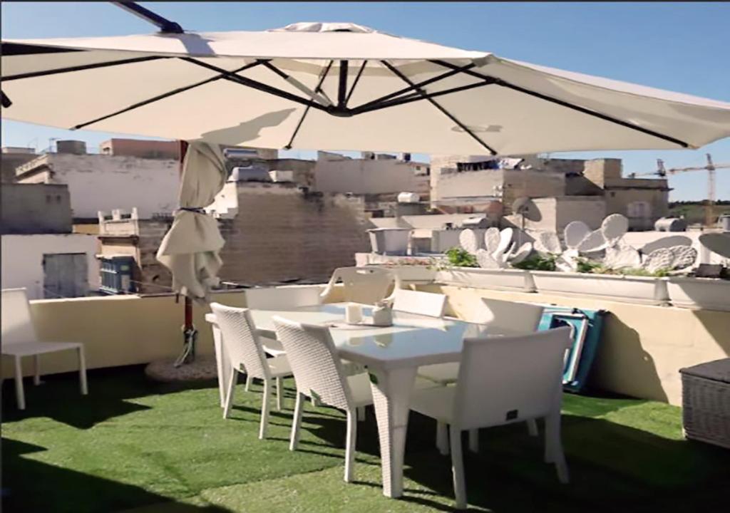 een witte tafel en stoelen onder een paraplu op een dak bij Corto Maltese Guest House in Cospicua