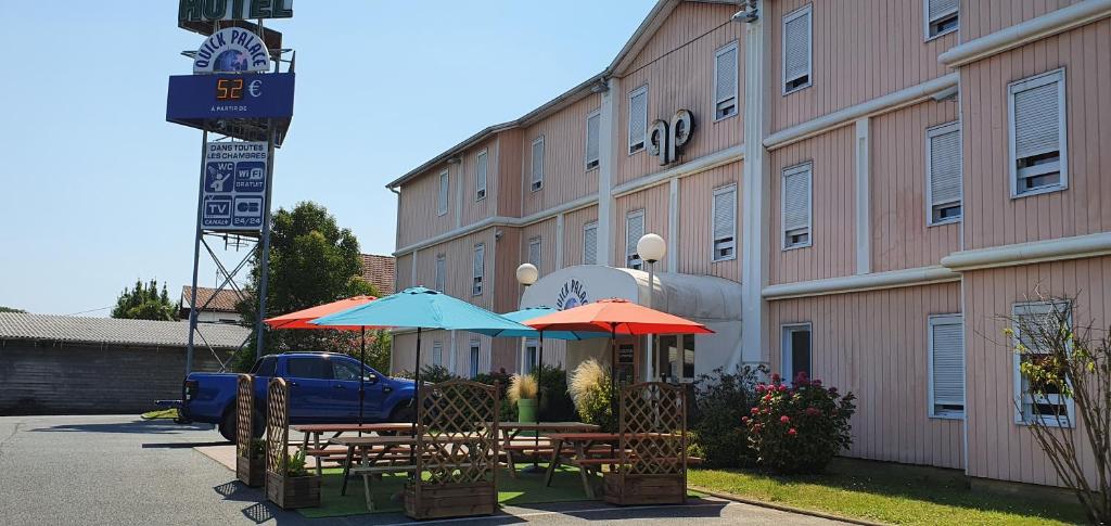 deux tables avec parasols devant un bâtiment dans l'établissement Quick Palace Anglet, à Anglet