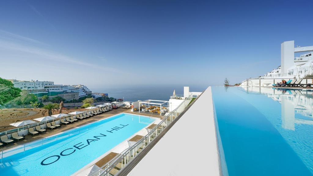 a pool on the side of a hotel with the ocean in the background at OCEAN HILL - Adults Only in Puerto Rico de Gran Canaria