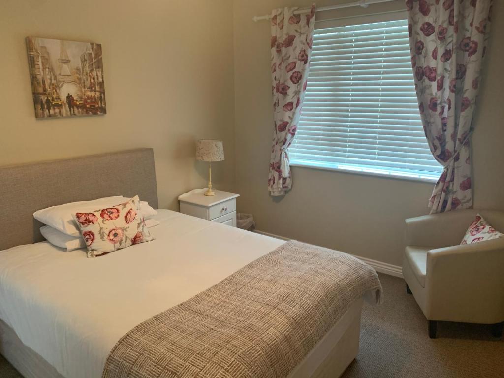 um quarto com uma cama, uma cadeira e uma janela em Oak Lodge Portumna em Portumna