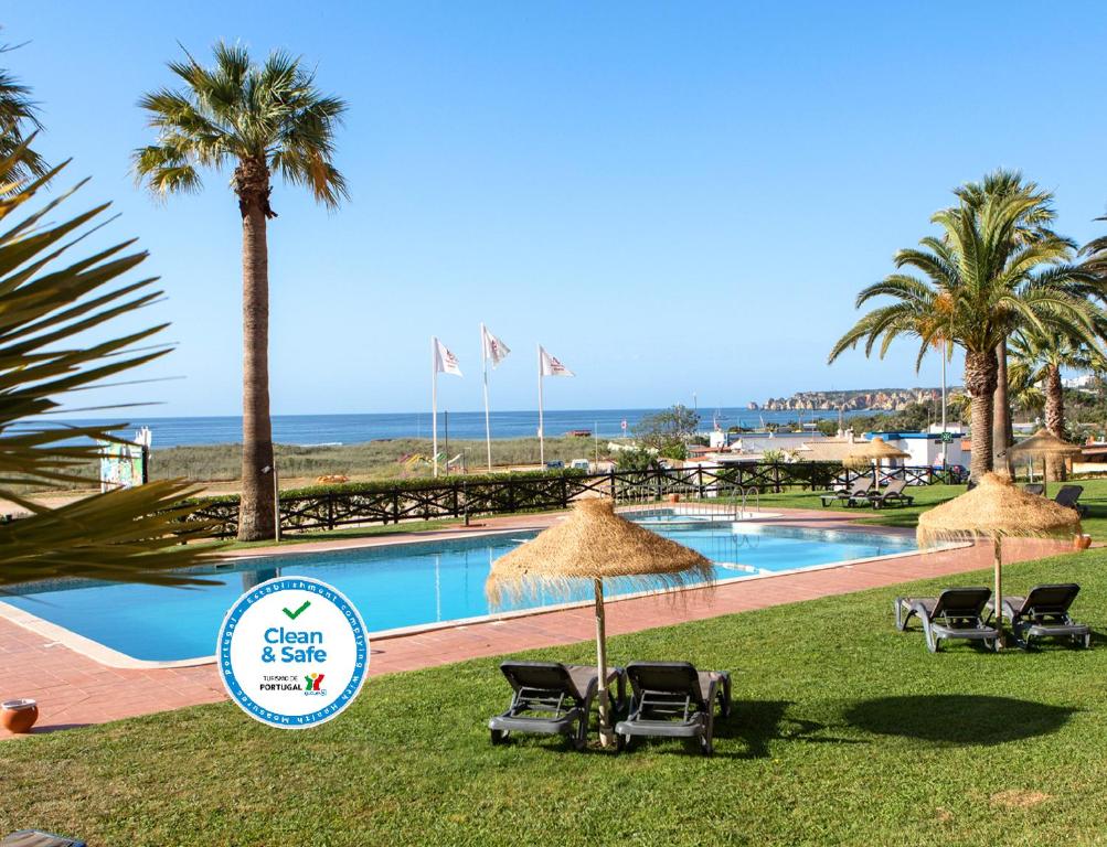 a pool with chairs and umbrellas and the ocean at Dom Pedro Lagos in Lagos