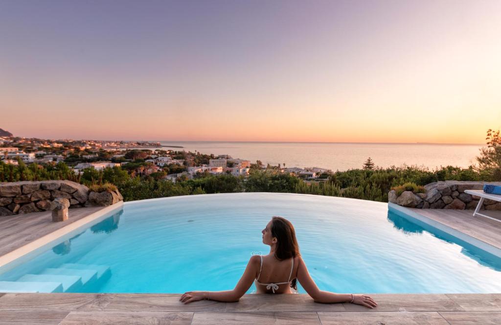 a woman sitting on the edge of a swimming pool overlooking the ocean at Villa dei Lecci - 7 Luxury villas with private pool or jacuzzi in Ischia