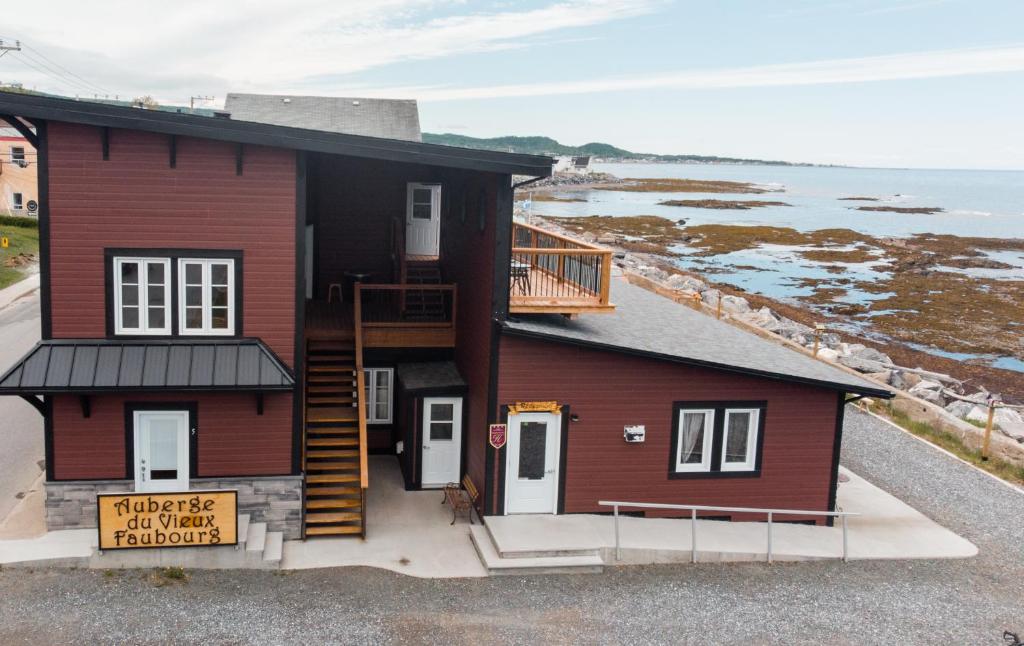 una casa rossa con balcone e oceano di Auberge du Vieux Faubourg a Sainte-Anne-des-Monts