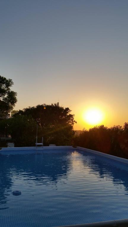 a swimming pool with the sunset in the background at Alexandra Homestay in Kalavárda