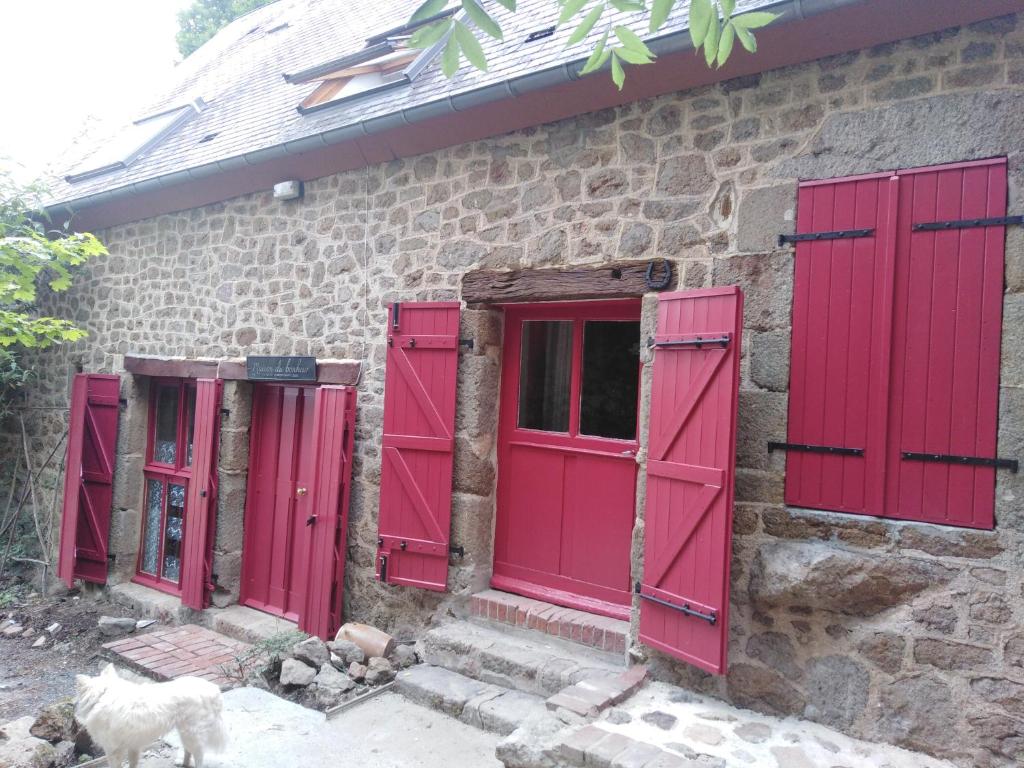 - un bâtiment en pierre avec des portes rouges et un chien debout devant dans l'établissement au petit bonheur, à Putanges