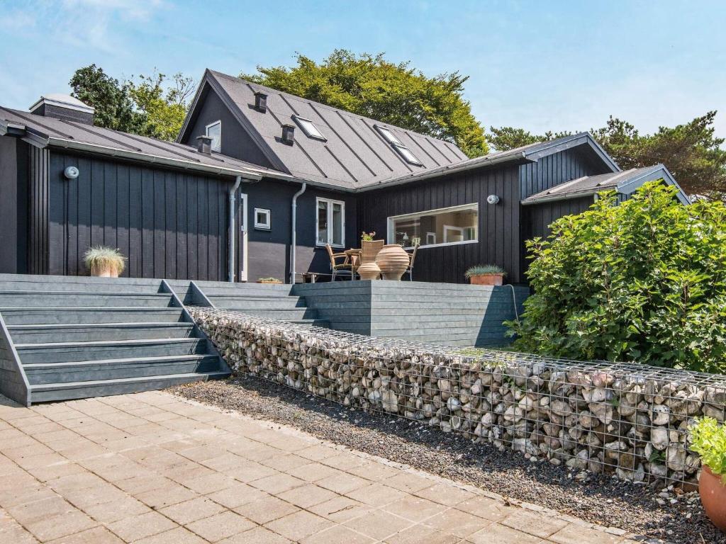 a black house with a stone retaining wall and stairs at 6 person holiday home in Bjert in Sønder Bjert