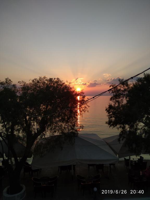 a sunset over the water with a tent and trees at Aktaion in Milina