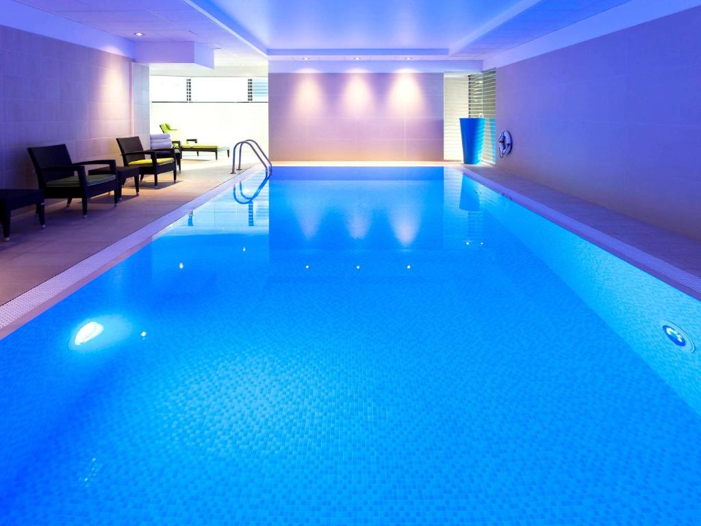 a large swimming pool with blue water in a room at Novotel London Paddington in London