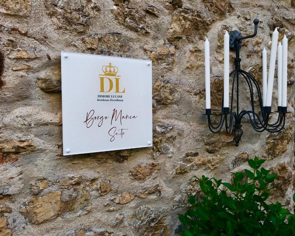 a sign on a stone wall with white candles at Borgo Manca Suite in Sasso di Castalda