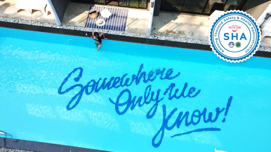 un homme debout à côté d'une piscine bleue avec un panneau dans l'établissement Bluemoon, à Cha Am