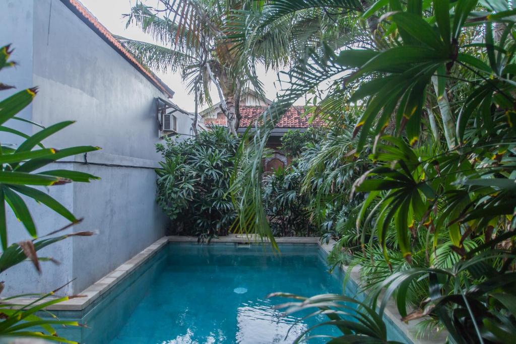 a swimming pool in a garden with palm trees at Sadana Bali Guesthouse in Sanur