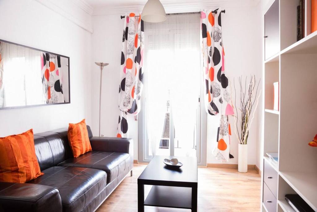 a living room with a black leather couch and orange pillows at Po Colorful and bright apartment in Barcelona