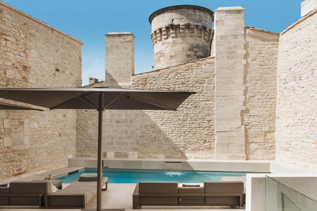 uma piscina com um guarda-sol em frente a um castelo em Hôtel de Tourrel, Saint Rémy de Provence, a Member of Design Hotels em Saint-Rémy-de-Provence