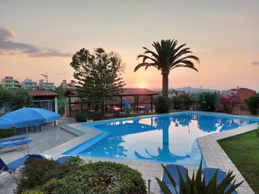 a swimming pool with a palm tree and a sunset at Argo Apartments in Kato Daratso