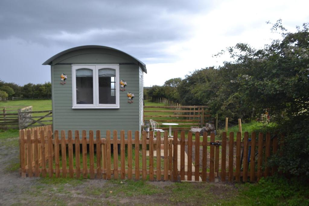 une petite maison verte derrière une clôture en bois dans l'établissement Peaceful Shepherd's Hut next to Horse Field, à Morpeth