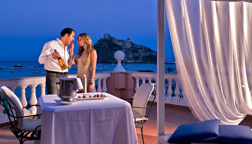 un homme et une femme debout sur un balcon avec une table dans l'établissement Hotel Mare Blu Terme, à Ischia