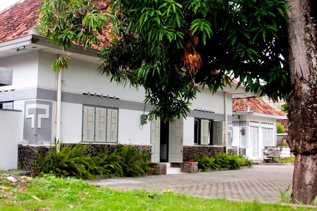 uma casa branca com uma árvore em frente em Ndalem Mantrigawen em Yogyakarta