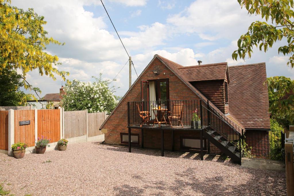 a small brick house with a deck and a balcony at Oakland Cottage in Craven Arms