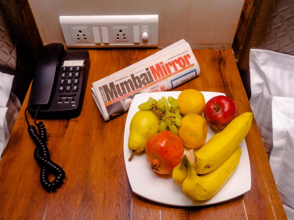 a plate of fruit on a table with a phone at Hotel Alfa Heritage in Mumbai