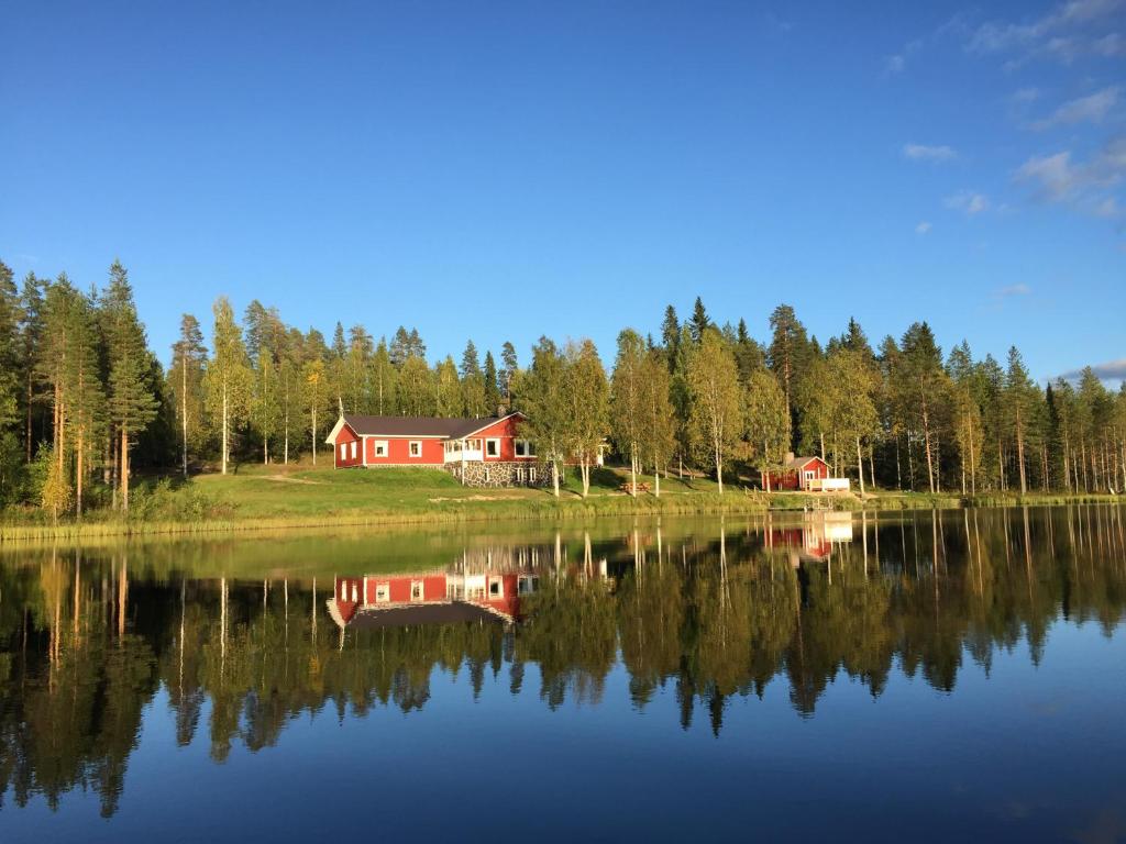 a red house is reflected in a lake at Hiiden Kämppäkartano iso vuokramökki lähellä Tiilikan kansallispuistoa in Sotkamo
