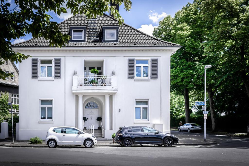 two cars parked in front of a white house at Design-Loft und Apartment im Villenviertel in Mülheim an der Ruhr
