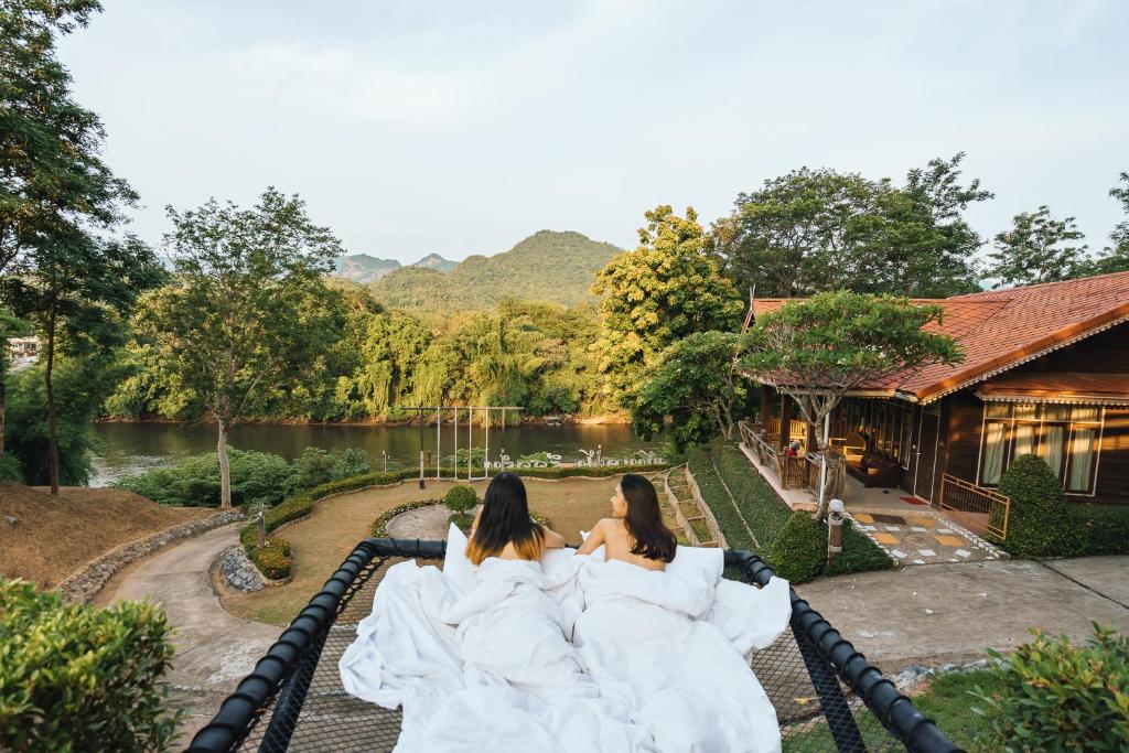 dos mujeres vestidas de blanco sentadas en una montaña rusa en Baanpufa Resort, en Sai Yok